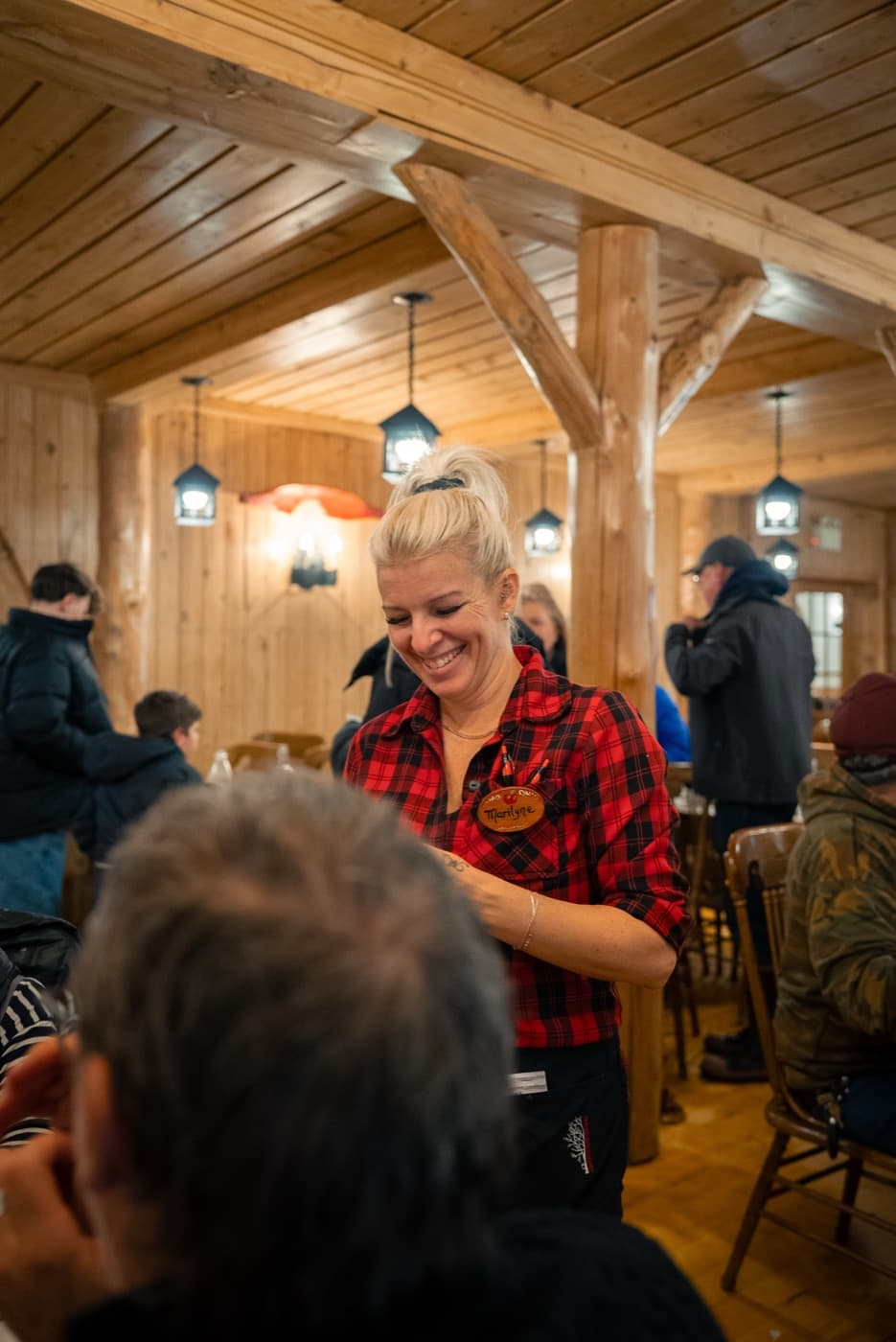 Serveuse souriante en chemise carreautée dans la salle à manger en bois de l'érablière